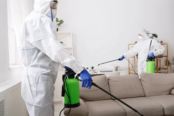 two people in hazmat suits spraying a living room with a cleaning substance