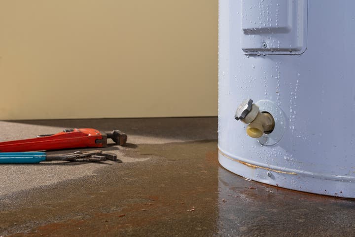 A Servpro technician is preparing to fix a water heater that is leaking water. The image shows water pooling around the base of the heater, indicating a significant leak.